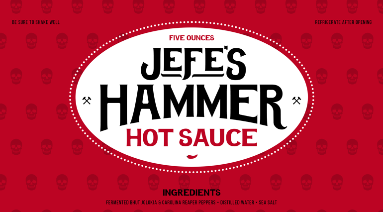 Sauce bottle red label with bespoke skull pattern in background and large black logo text sitting inside white circle in center
