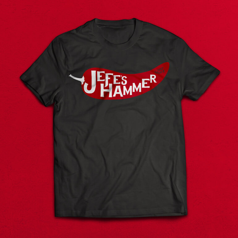 Black t-shirt with red pepper and white text printed on it, sitting on a red background