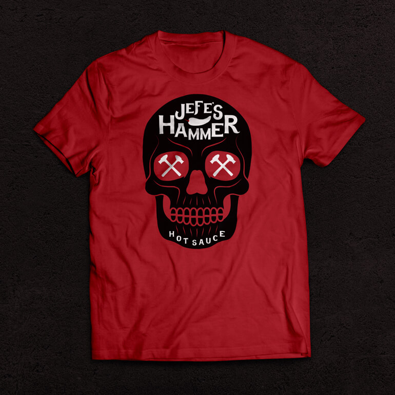 Red t-shirt with black skull and white text printed on it, sitting on a black background